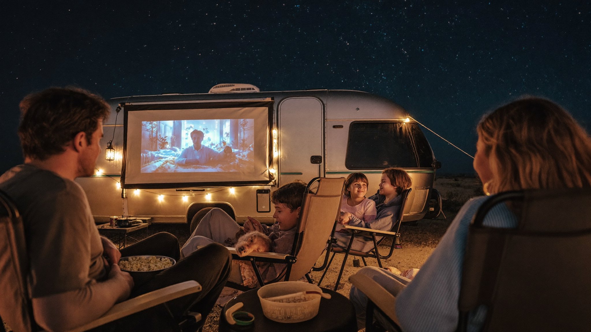 Kids watching a film on a screen rigged to the trailer under a starry desert sky